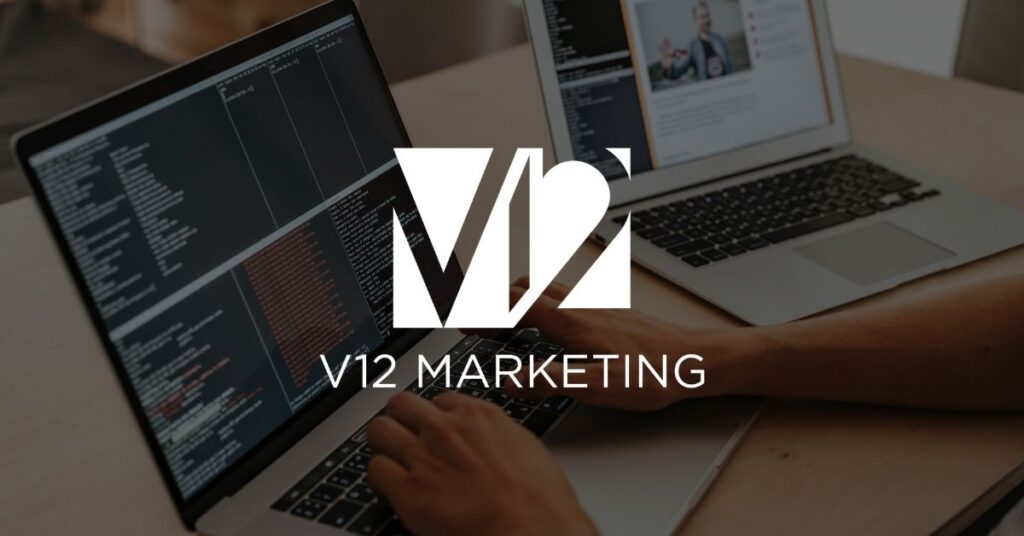 Developer typing code on a laptop next to a second laptop showing a website design, with the V12 Marketing logo overlaid.